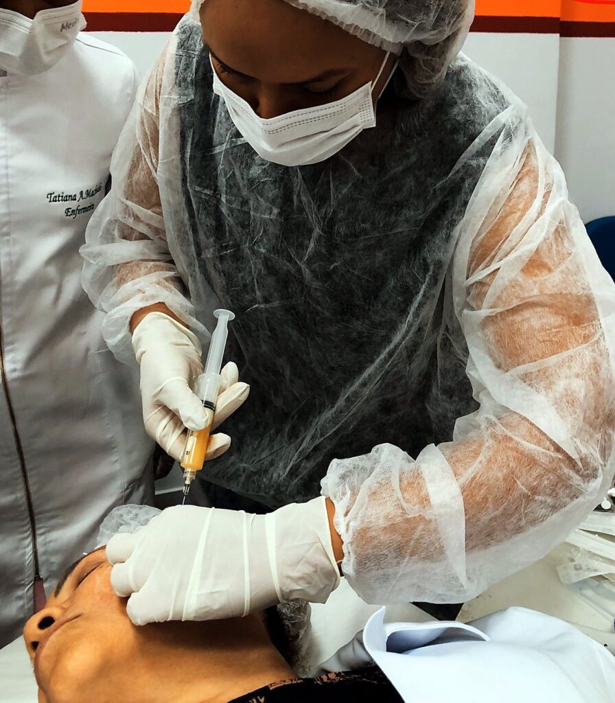 Aluna faz aplicação facial em paciente real na pós em Estética Avançada, com EPI completo